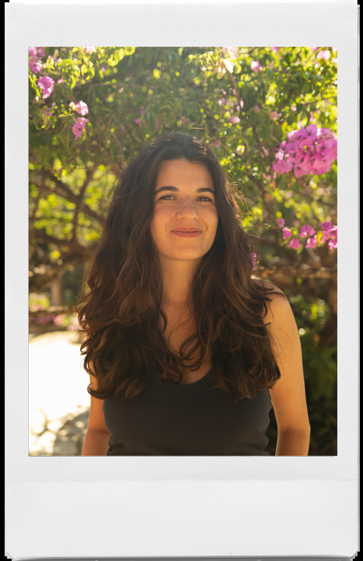 Lavínia Pedrosa sorrindo em um jardim com flores cor-de-rosa ao fundo, em moldura polaroid